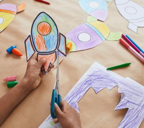 Close up of hands cutting out a craft paper rocketship