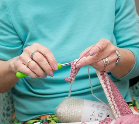 Close up of hands doing a crochet project with pink and white yarn