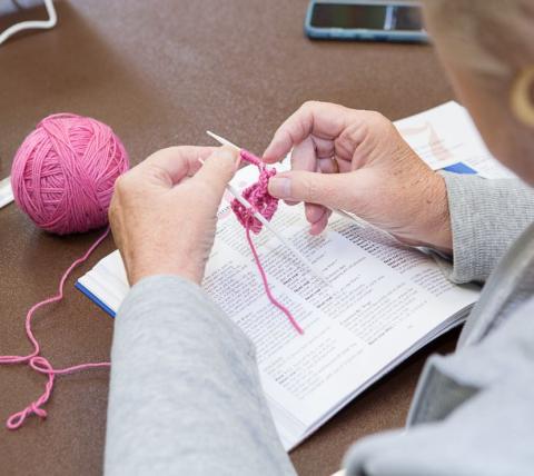 close up of hands knitting with pink yarn