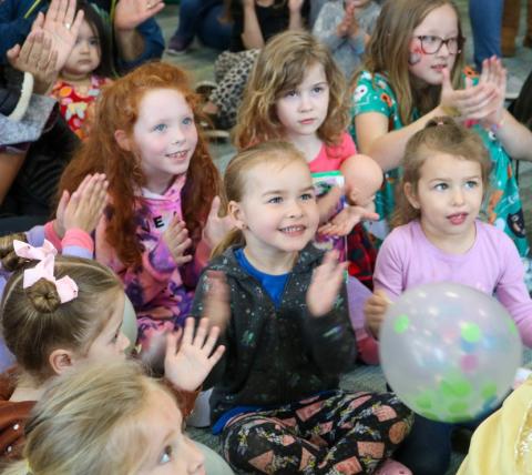 happy smiling kids sitting down for story time and clapping along with story time leader