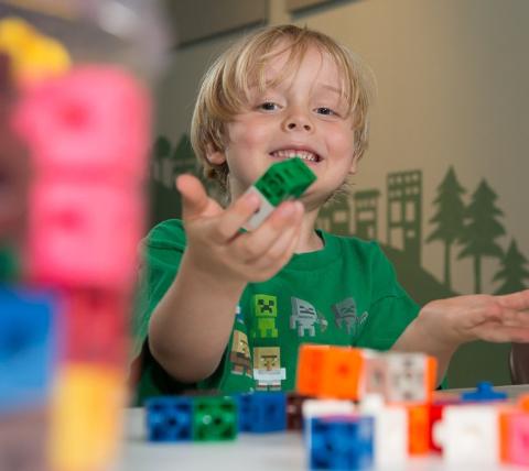 little boy holding colorful blocks up to the camera smiling