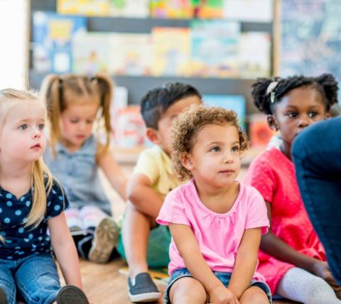 diverse children sitting on a carpet listening to a story