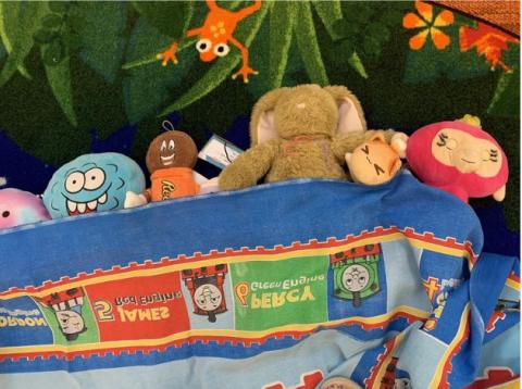 stuffed animals laying on a colorful carpet covered with a train sheet