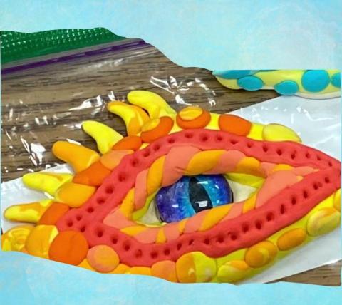 close up of a children's clay craft. The clay is shaped to look like a close-up of a dinosaur eye