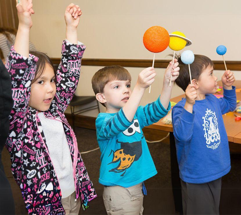 three children holding up models of planets