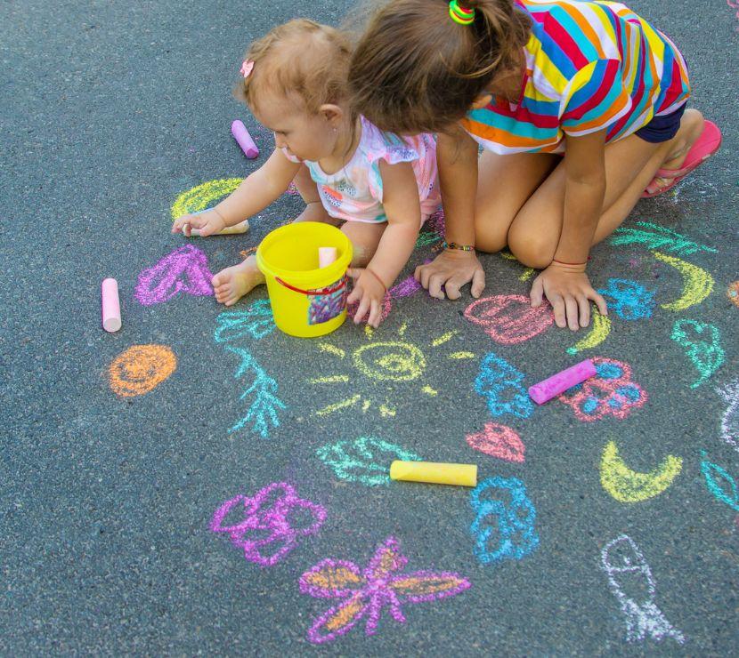 baby and school age child kneeling on the sidewalk drawing with colorful chalk