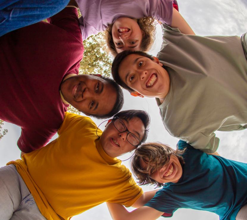 5 adults in a group huddle looking down excitedly.